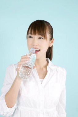 Mavi arka planda bir şişe suyu olan güzel, genç Asyalı bir kadın.