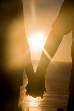 Gün batımında kumsalda el ele tutuşan mutlu çiftin silueti. 