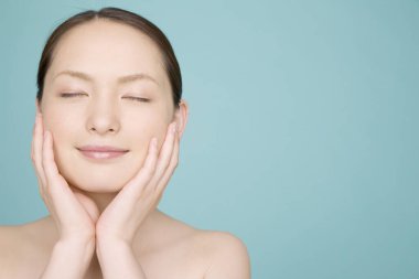 Mavi arka planda gözleri kapalı Asyalı genç bir kadın.