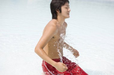 Mutlu Asyalı genç adam yüzme havuzunda eğleniyor.