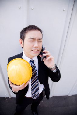 İnşaat alanında kasklı Asyalı bir işadamı telefonda konuşuyor.