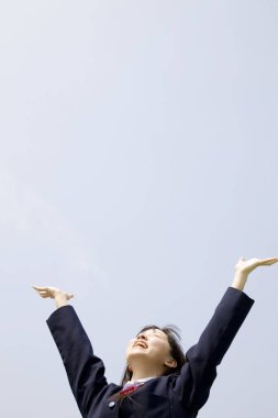 Okul üniformalı güzel Japon kızın portresi ellerini mavi gökyüzü arka planına kaldır.