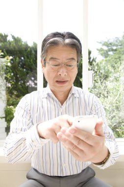 Evde akıllı telefon kullanan yakışıklı, olgun bir Japon 'un portresi.