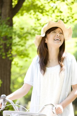 Bisikletli ve hasır şapkalı Asyalı kadın yaz günü parkta