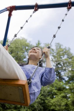 Genç Asyalı kadın parkta salıncakta oturuyor.