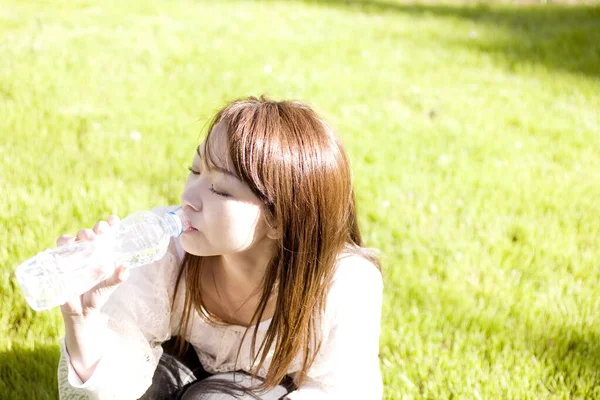 Attraktiv Ung Asiatisk Kvinna Dricksvatten Från Flaska Och Sitter Gräs — Stockfoto