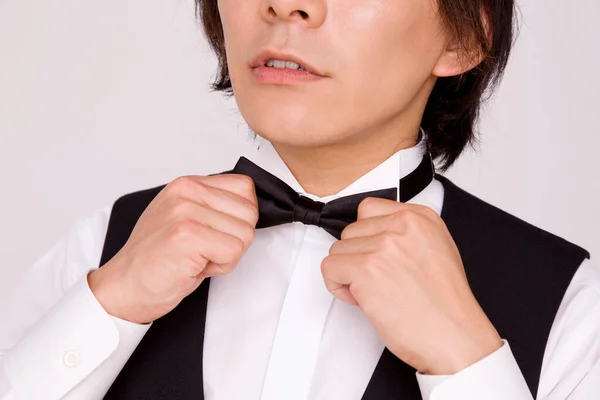 Close up view of Asian waiter adjusting bow tie on studio background