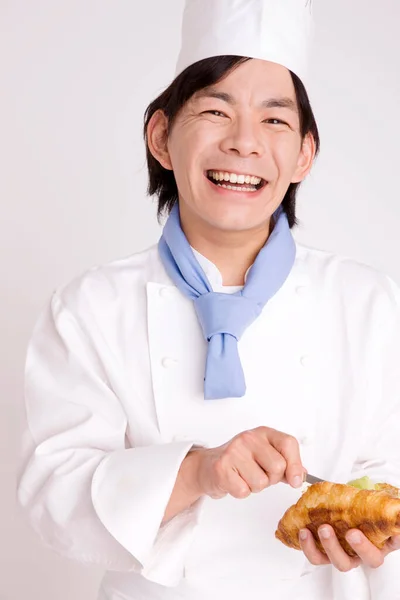 Uśmiechnięty Azjatycki Kucharz Cięcia Świeże Rogaliki Nożem — Zdjęcie stockowe