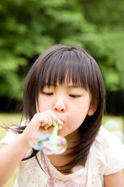 夏の公園で石鹸の泡を吹く小さなアジアの少女 — ストック写真