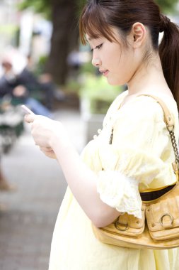 Parkta akıllı telefon kullanan gülümseyen Asyalı kadın.  