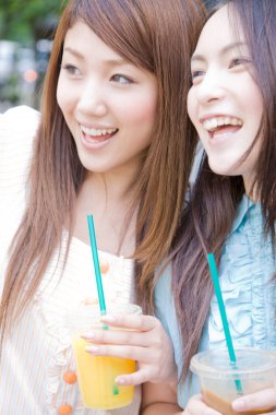 Parkta kokteyl içen iki genç kadının portresi.