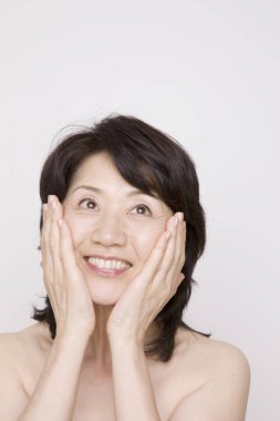 Yüzünde elleri olan Asyalı olgun bir kadının portresi. 