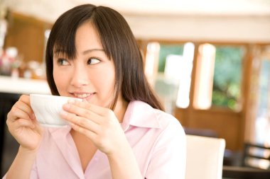 Kafede bir fincan kahve içen genç Asyalı kadın.