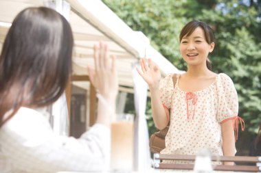 Genç Asyalı kadınlar açık kafede birbirlerine el sallıyorlar. 