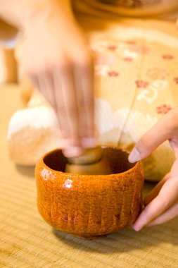 Geleneksel kimono giyen Asyalı bir kadının elinde ahşap bir fincan çay tutarken çekilmiş bir fotoğrafı. 
