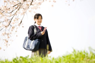 Çiçek açan sakura ağacının üzerinde poz veren güzel ve tatlı Japon okul kızının portresi.