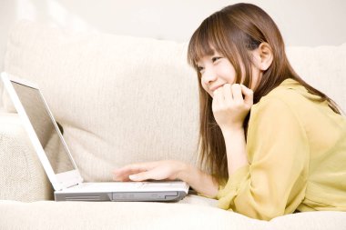 Güzel Asyalı kadın gülümsüyor ve evde laptop kullanıyor. 