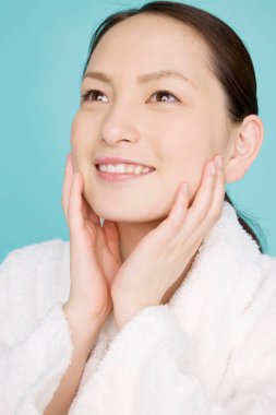 Bornozlu güzel bir Asyalı kadın mavi arka planda tek başına gülümsüyor.