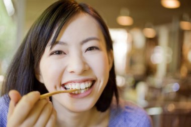 Kahvede çatalla yemek yiyen gülümseyen Japon kadın.