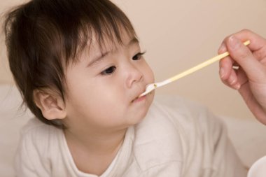 Annesi sevimli Asyalı bebeğini kaşıkla besliyor. 