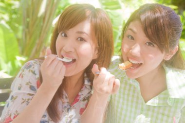 Parkta tatlı yiyen iki Asyalı mutlu arkadaş. 