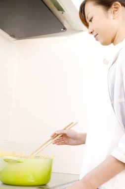 Genç bir kadın mutfakta çubuklarla makarna pişiriyor.