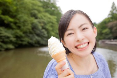 Neşeli Japon kadın gündüz vakti yeşil yaz parkında dondurma yiyor. 