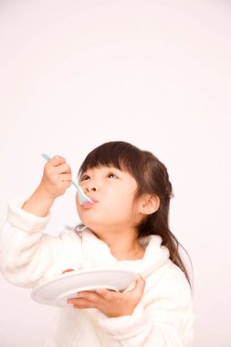 Beyaz stüdyo arka planında beyaz kremalı ve çilekli pasta yiyen küçük Japon kız.