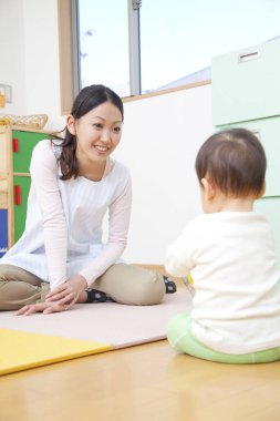 Küçük tatlı çocuk Japon anaokulunda öğretmenle oynuyor.