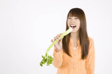 gülümseyen genç Asyalı kadın beyaz arka planda kereviz sapı yiyor.