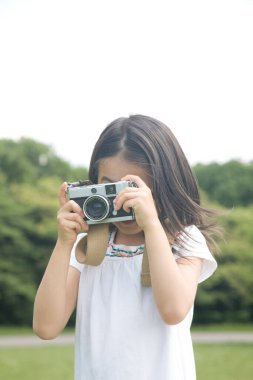 Küçük Asyalı kız dışarıda fotoğraf makinesi kullanıyor.