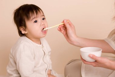 Annesi sevimli Asyalı bebeğini kaşıkla besliyor. 