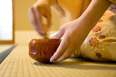 Geleneksel kimono giyen Asyalı bir kadının elinde ahşap bir fincan çay tutarken çekilmiş bir fotoğrafı. 