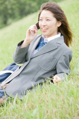 Yaz parkında cep telefonu olan Asyalı genç bir öğrencinin portresi.