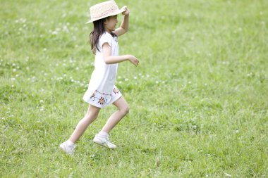 Yeşil çayırlarda koşan hasır şapkalı Asyalı küçük kız