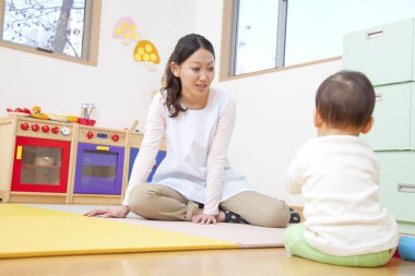 Küçük tatlı çocuk Japon anaokulunda öğretmenle oynuyor.