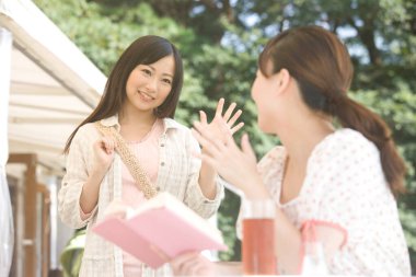 Genç kadınlar açık kafede birbirlerine el sallıyorlar. 