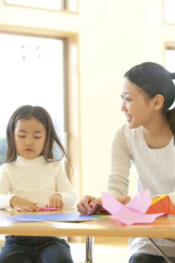 Genç bayan öğretmen ve tatlı Asyalı küçük kız Japon anaokulunda kağıt origami yapıyorlar.