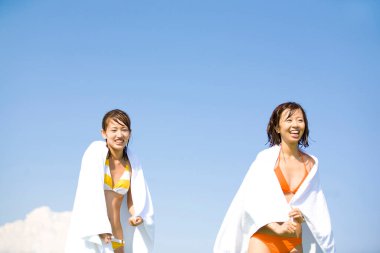 Sahilde havluları olan bikinili iki mutlu Asyalı kadın. 