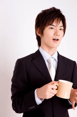 Asyalı genç bir işadamı arka planda bir kupa tutuyor. 