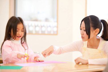 Genç bayan öğretmen ve tatlı Asyalı küçük kız Japon anaokulunda kağıt origami yapıyorlar.