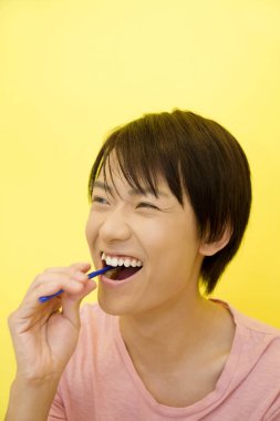  Asyalı bir adam sarı arka planda dişlerini fırçalıyor. 