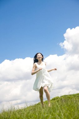 Yeşil çimenlerde koşan güzel, mutlu genç Japon kadının alçak açılı görüntüsü.