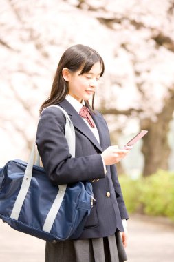 Çiçek açan kiraz ağacının arka planında okul üniformalı güzel Japon kızın portresi.