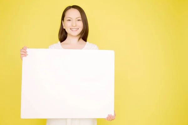 照片上美丽的日本女人举着空白的横幅 对着被黄色背景隔开的相机微笑 — 图库照片