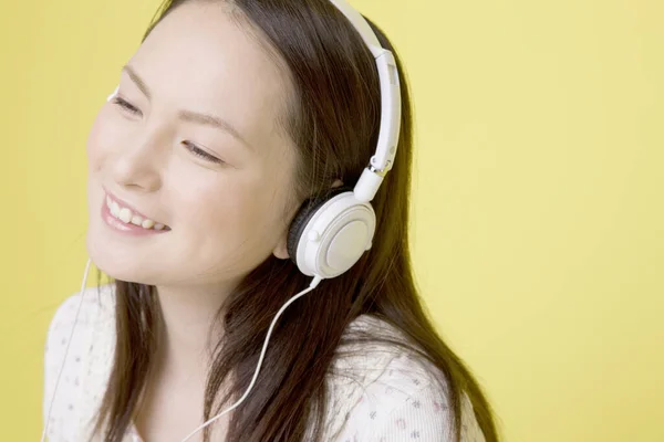 用黄色背景隔离的耳机听音乐的漂亮日本女人的肖像 — 图库照片