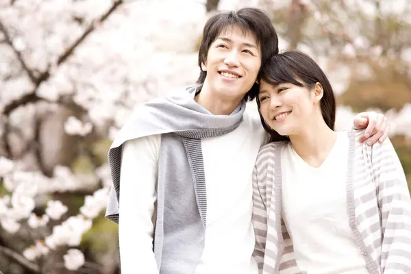 幸せな若い日本のカップルの肖像画は桜の花の間に公園で一緒に過ごしました — ストック写真