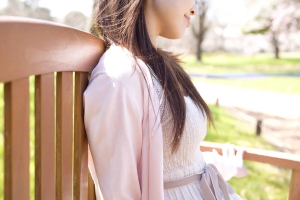 坐在公园长椅上的年轻貌美的亚洲女人的侧视图 — 图库照片