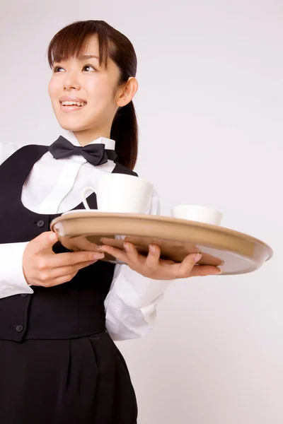 亚洲的年轻女服务员 餐盘上有杯子 背景偏僻 — 图库照片