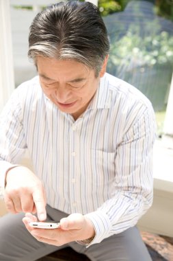 Evde akıllı telefon kullanan yakışıklı, olgun bir Japon 'un portresi.